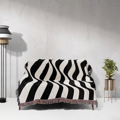 Black and white accent abstract waves woven blanket throw tapestry draped over a sofa against a light gray wall.