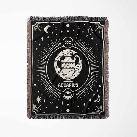 Displayed in a flat vertical orientation, the Aquarius Zodiac Blanket showcases its detailed zodiac design. The Aquarius symbol is prominently featured in the center, with an array of celestial motifs encircling it. The blanket's multicolor fringe complements the black and off-white woven pattern, enhancing its visual appeal.