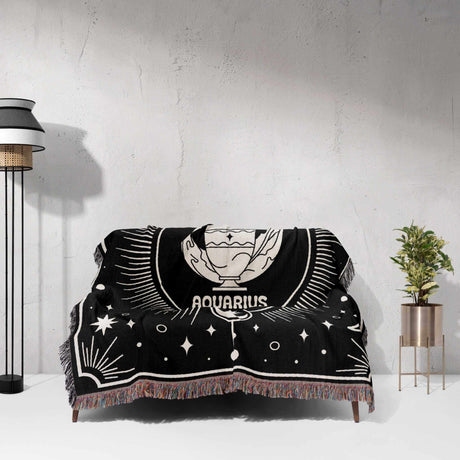 The Aquarius Zodiac Blanket is shown draped over a couch in this image. The detailed zodiac design and the vibrant multicolor fringe create a stunning contrast against the couch, highlighting the blanket's aesthetic and practical qualities. The celestial motifs surrounding the Aquarius symbol add a touch of mystique to the living space.