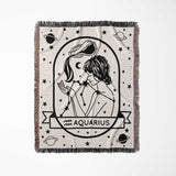 This image shows a horizontal flat lay of the Aquarius Zodiac Sign Blanket. The woven tapestry blanket features a black-and-white design of an Aquarius woman, adorned with celestial and constellation motifs. Perfect for adding a personalized touch to any room, it combines comfort with astrological elegance.