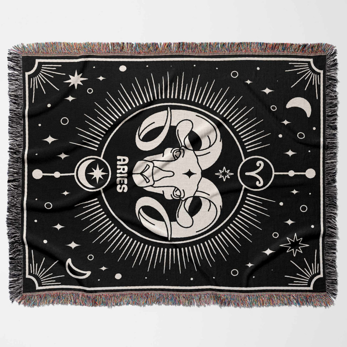 This image displays the Aries Zodiac Blanket laid flat in a horizontal position. The design features a prominent Aries symbol at the center with detailed zodiac elements and patterns surrounding it. The multicolor fringe adds a vibrant touch to the edges of the black and off-white blanket.