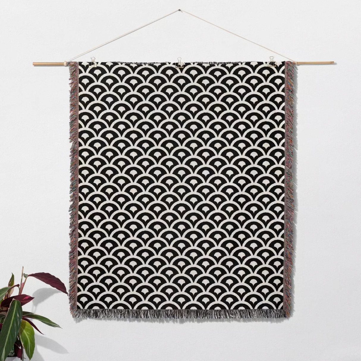 Black and white asian geometric pattern woven blanket throw tapestry hanging on a white wall with a plant in the corner.
