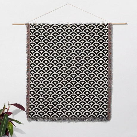 Black and white asian geometric pattern woven blanket throw tapestry hanging on a white wall with a plant in the corner.