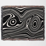 Black and white abstract woven throw blanket with fringe on a light gray background
