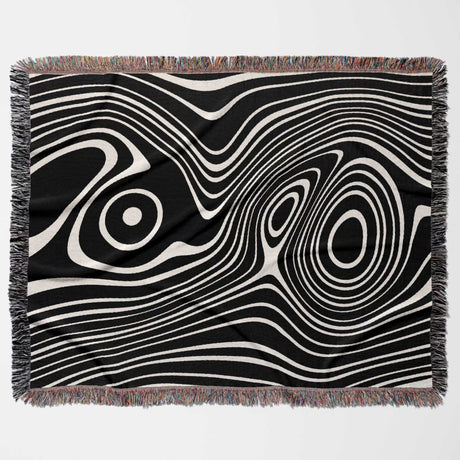 Black and white abstract woven throw blanket with fringe on a light gray background