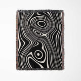 Black and white abstract woven throw blanket with fringe on a light gray background.