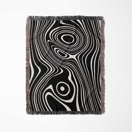 Black and white abstract woven throw blanket with fringe on a light gray background.