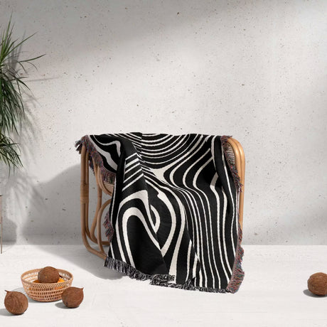 Black and white abstract woven throw blanket draped over a wooden chair against a light gray wall.