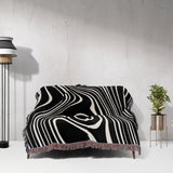 Black and white abstract woven throw blanket draped over a sofa against a white wall.