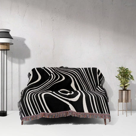 Black and white abstract woven throw blanket draped over a sofa against a white wall.