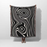 Person holding a black and white abstract woven throw blanket against a white background