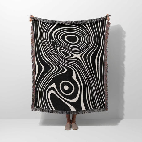Person holding a black and white abstract woven throw blanket against a white background