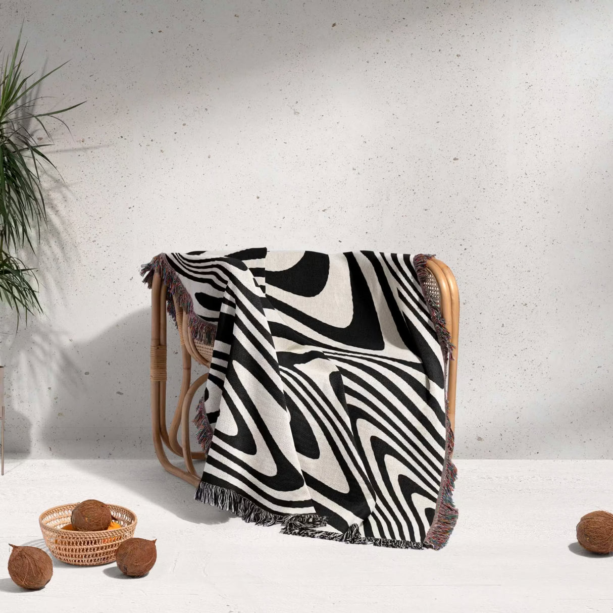 Black and white modern couch woven throw blanket draped over a wooden chair on a light gray background.