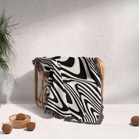Black and white modern couch woven throw blanket draped over a wooden chair on a light gray background.