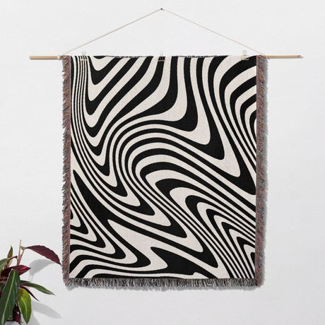 Black and white modern couch woven throw blanket hanging on a wooden rod against a white wall.