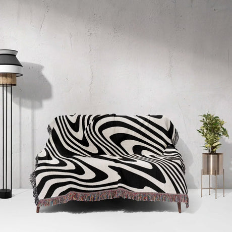 Black and white modern couch woven throw blanket on a sofa against a white wall.