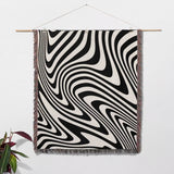 Black and white modern decorative woven throw blanket hanging on a wooden rod against a white wall.