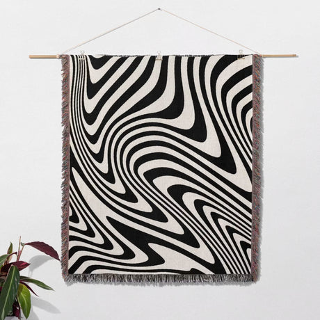Black and white modern decorative woven throw blanket hanging on a wooden rod against a white wall.