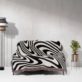 Black and white modern decorative woven throw blanket on a sofa against a white wall.