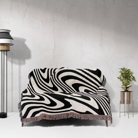 Black and white modern decorative woven throw blanket on a sofa against a white wall.