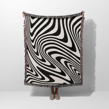 Person holding a black and white modern decorative woven throw blanket against a white background