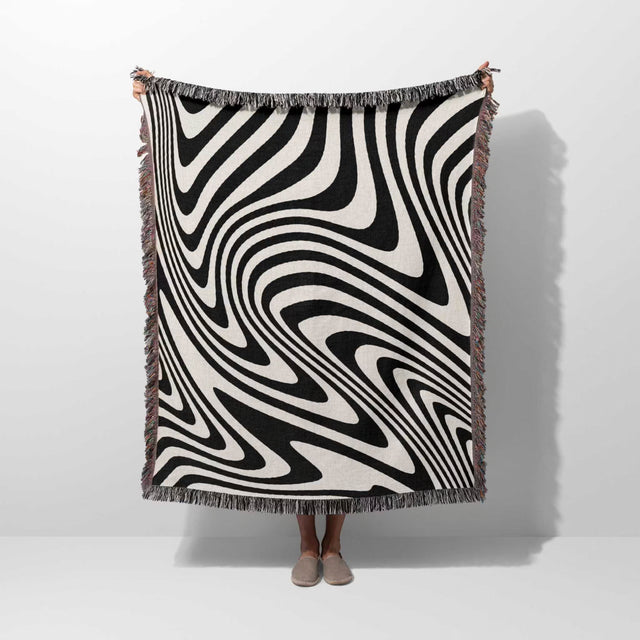 Person holding a black and white modern decorative woven throw blanket against a white background