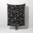 Black blanket with white abstract patterns draped over a person on a white background