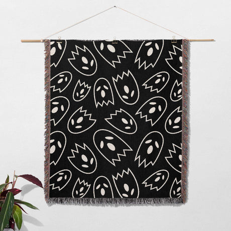 Black blanket with white abstract patterns hanging on a wooden rod against a white wall.