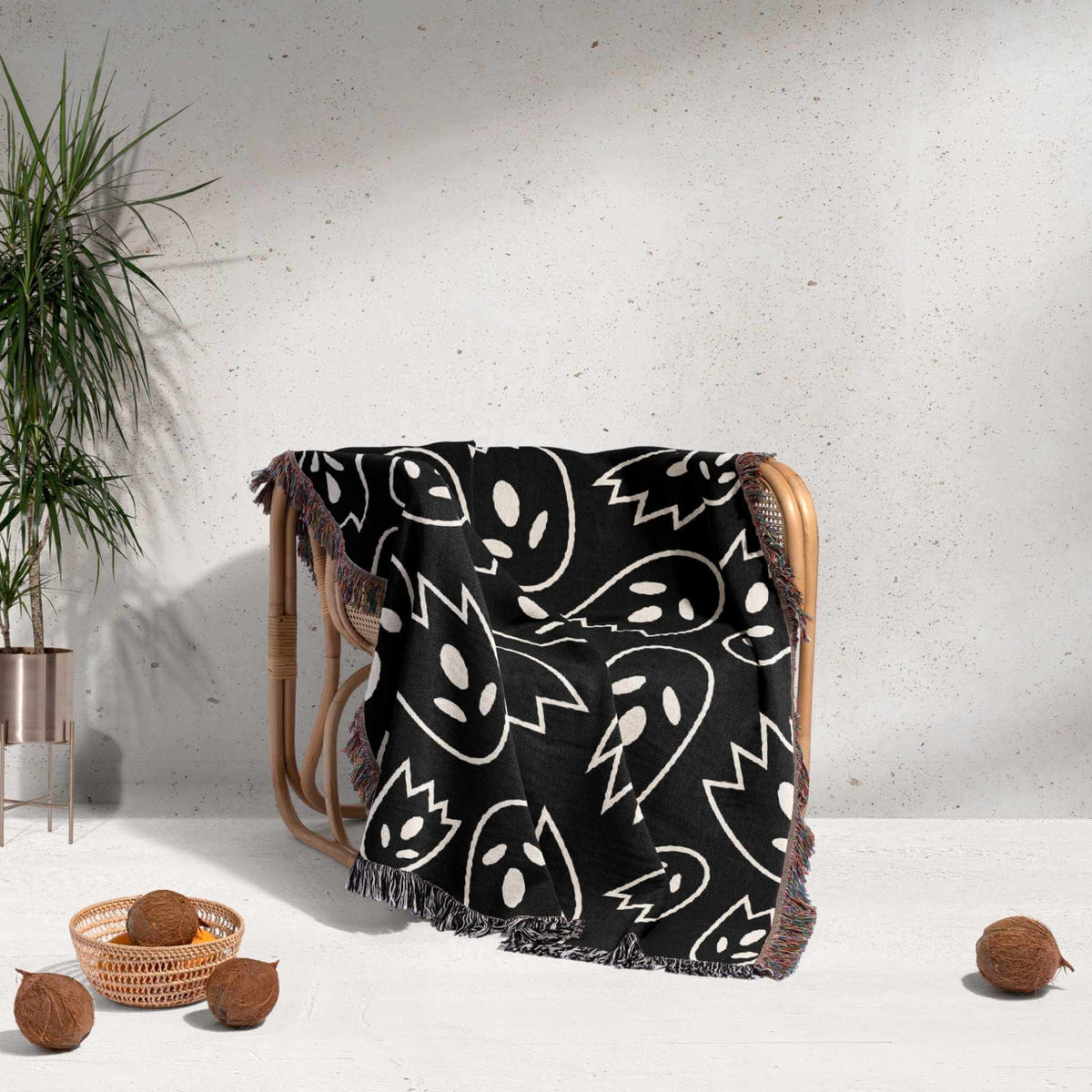 Black blanket with white patterns draped over a chair against a light gray wall.