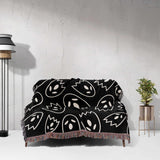 Black blanket with white abstract patterns draped over a sofa against a light gray wall.