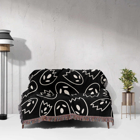 Black blanket with white abstract patterns draped over a sofa against a light gray wall.
