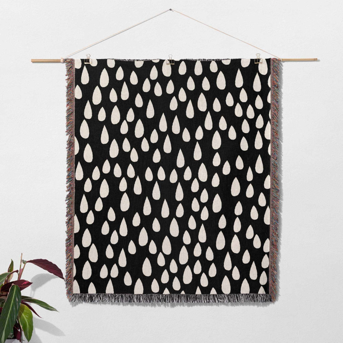 Black blanket with white teardrop pattern hanging on a wooden rod against a white wall.