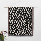 Black blanket with white teardrop pattern hanging on a wooden rod against a white wall.
