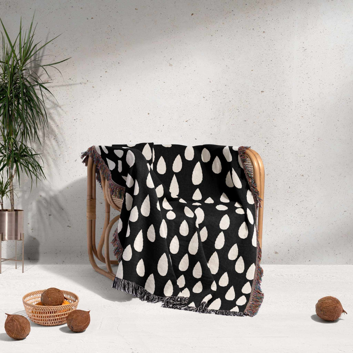 Black and white patterned blanket draped over a chair with a plant and coconuts in the background.