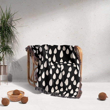 Black and white patterned blanket draped over a chair with a plant and coconuts in the background.