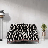 Black and white patterned blanket draped over a sofa against a light gray wall.
