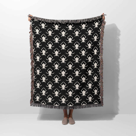 Black blanket with white spider pattern draped over a person on a white background.