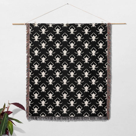 Black and white Geometric Spiders Pattern Woven Throw Blanket hanging on a wooden rod against a white background.