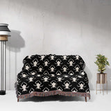 Black and white geometric spiders pattern woven throw blanket draped over a sofa against a light gray wall.