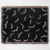 The black and white Halloween blanket is laid out flat, showcasing its bat pattern design. The blanket features a repeating pattern of white bats on a black background, bordered with a multicolored fringe.