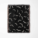 The black and white Halloween blanket is displayed in a vertical position, revealing its full bat pattern design. The image captures the contrast between the white bat silhouettes and the dark background, with fringes visible at the edges.