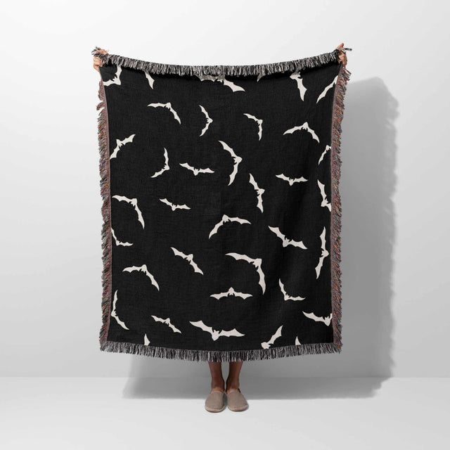 A person is holding up the Halloween blanket vertically, showcasing its bat pattern design. The size of the blanket is fully visible, emphasizing its use as a cozy throw for Halloween décor.