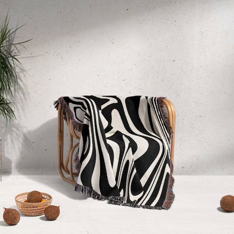 Black and white marble woven throw blanket for couch draped over a wooden chair against a light gray wall.