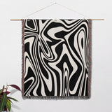 Black and white marble woven throw blanket for couch hanging on a wooden rod against a white wall.