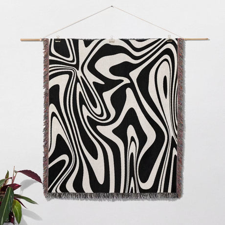 Black and white marble woven throw blanket for couch hanging on a wooden rod against a white wall.