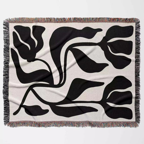 Black and white Matisse flower woven throw blanket floral pattern on a beige blanket with fringe flat on the floor