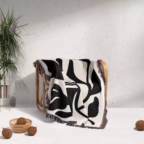 Black and white Matisse flower woven throw blanket patterned draped over a chair against a light gray wall.