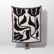 Person holding a black and white Matisse flower woven throw blanket against a white background
