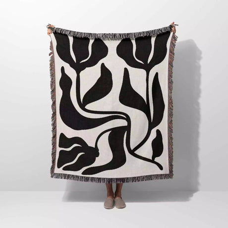 Person holding a black and white Matisse flower woven throw blanket against a white background