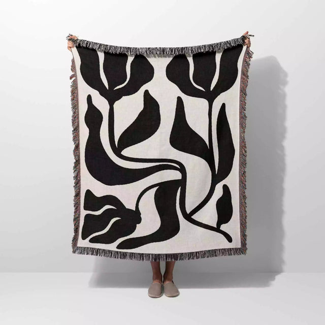 Person holding a black and white Matisse flower woven throw blanket against a white background